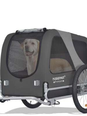 Ein Hund sitzt in einem grauen Doggyhut-Fahrradanhänger mit Netzfenstern und einer kleinen orangefarbenen Sicherheitsflagge.